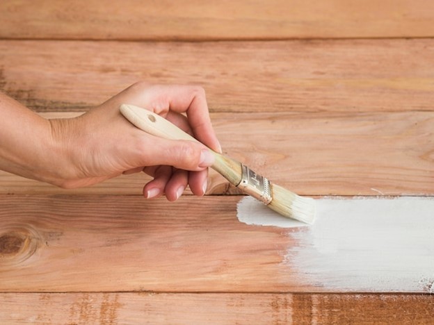 A person applying vinyl glue on the subfloor to install planks.